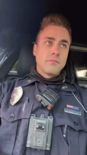 A Police Officer Is Sitting In A Car With A Walkie Talkie On His Chest GIF