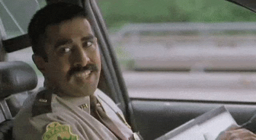 A Police Officer Is Sitting In The Driver 'S Seat Of A Car Holding A Piece Of Paper . GIF