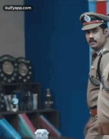 A Police Officer Is Standing In A Room With A Lot Of Trophies On The Shelf . GIF