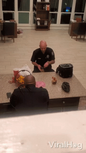 A Police Officer Sits At A Counter With Another Officer GIF