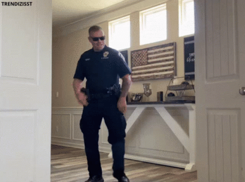 A Police Officer Standing In Front Of A Door With Trendizisst Written On It GIF