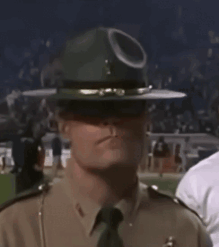 A Police Officer Wearing A Hat And Sunglasses Is Standing In A Crowd . GIF