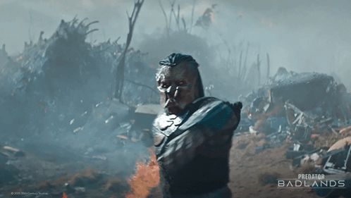 A Poster For Predator Badlands Shows A Man Standing In A Pile Of Trash GIF