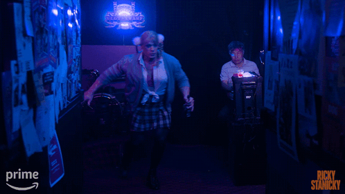 A Poster For Ricky Stanicky Shows A Man In A Plaid Skirt In A Dark Hallway GIF