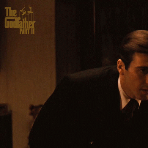 A Poster For The Godfather Part Ii Shows A Man In A Suit And Tie Sitting On A Couch GIF