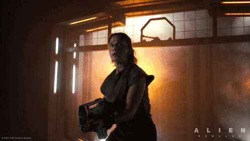 A Poster For The Movie Alien Romulus With A Woman Holding A Gun GIF