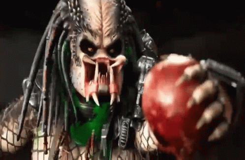 A Predator Is Holding A Red Apple With His Mouth Open . GIF