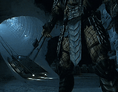 A Predator Is Standing In A Tunnel Holding A Spear GIF
