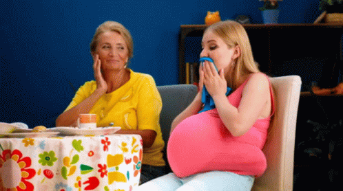 A Pregnant Woman Is Sitting At A Table With A Floral Tablecloth GIF