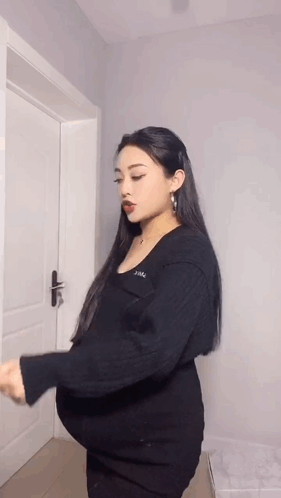A Pregnant Woman Is Standing In Front Of A Door Holding Her Belly . GIF