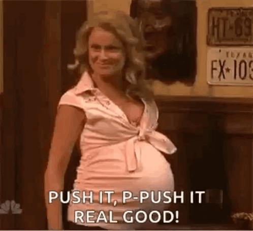 A Pregnant Woman Is Standing In Front Of A Sign That Says Push It , P - Push It Real Good . GIF
