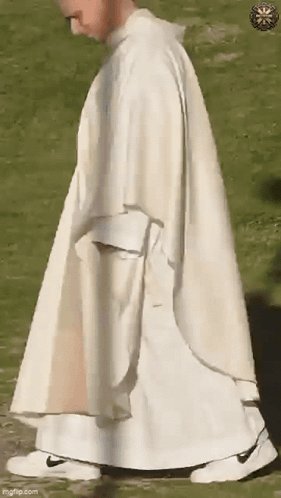 A Priest In A White Robe And White Sneakers Is Walking In A Field . GIF