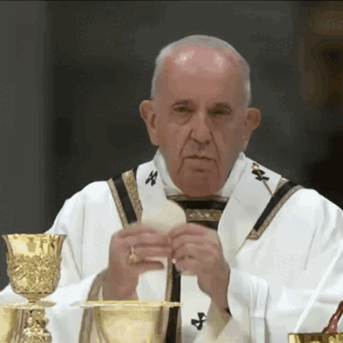 A Priest Is Holding A Piece Of Bread In Front Of A Chalice GIF
