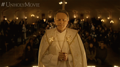 A Priest Is Praying In Front Of A Crowd With #Unholymovie Written On The Bottom Right GIF