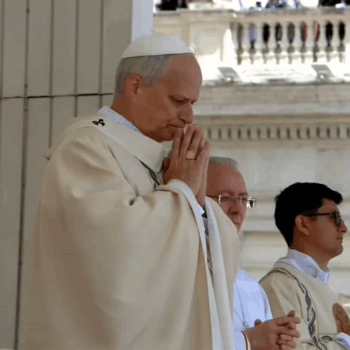A Priest Is Praying With His Hands Folded In Front Of A Balcony GIF