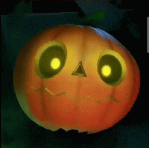 A Pumpkin With Glowing Eyes And A Face Carved Into It Is Sitting On A Table . GIF