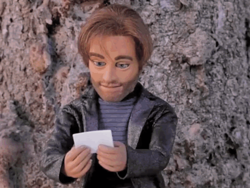 a puppet is leaning against a tree and holding a piece of paper