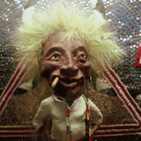 A Puppet With A Cigarette In His Mouth Is Wearing A White Shirt And Necklaces GIF