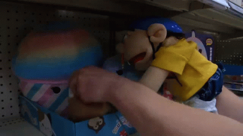 A Puppet With A Pencil In His Mouth Is Sitting On A Shelf In A Store .. GIF