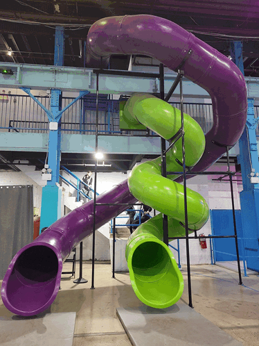 A Purple And Green Slide In A Building With Stairs GIF