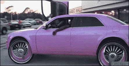 A Purple Car With Big Wheels Is Parked In A Lot GIF