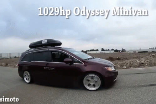 A Purple Minivan With A Roof Box On Top Is Driving Down A Road GIF