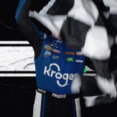 A Race Car Driver Wearing A Kroger Jersey Holds A Checkered Flag GIF