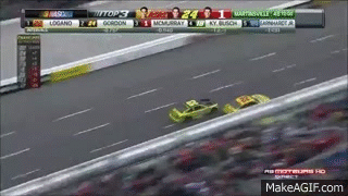 A Race Car Is Driving Down A Race Track With A Scoreboard Behind It . GIF