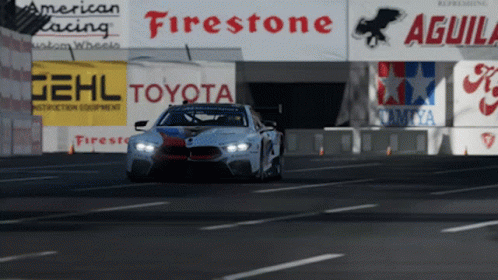 A Race Car Is Driving Down A Road In Front Of Signs For Firestone Toyota And Aguila GIF
