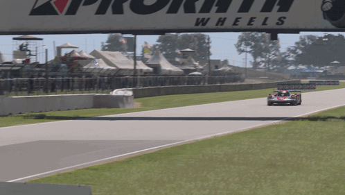 A Race Car Is Driving Down A Track Under A Sign That Says Wheels GIF