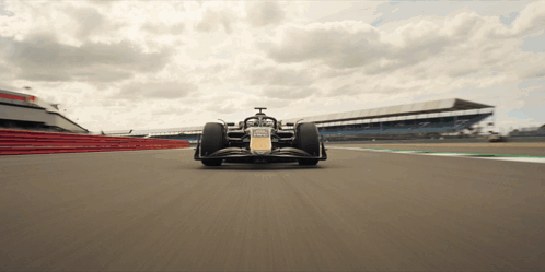 A Race Car Is Driving Down A Track With A Large Building In The Background GIF