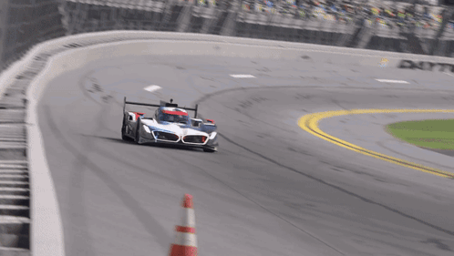 A Race Car Is Driving Down A Track With A Red And White Cone In Front Of It GIF