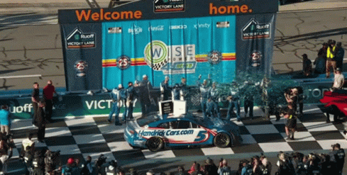 A Race Car Is On A Checkered Race Track With A Banner That Says Welcome Home GIF
