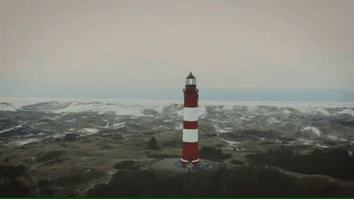 A Red And White Lighthouse Sits On Top Of A Hill GIF