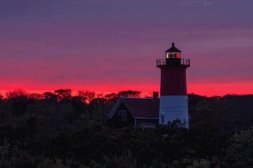 A Red And White Lighthouse Stands In Front Of A Sunset Sky GIF