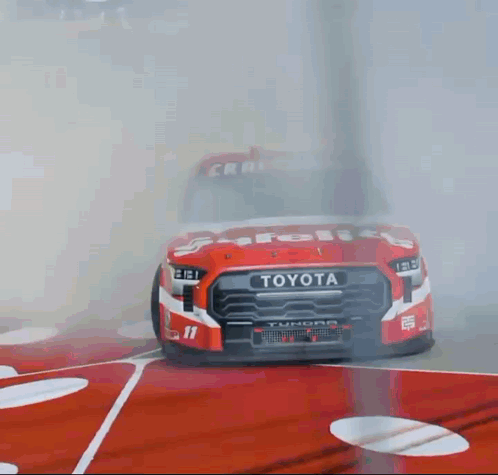 A Red And White Toyota Truck Is Driving On A Race Track GIF