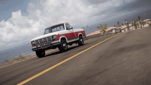 A Red And White Truck Is Driving Down A Road Near The Ocean GIF