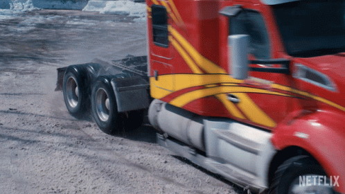 A Red And Yellow Semi Truck Is Driving Down A Dirt Road With Netflix Written On The Bottom GIF