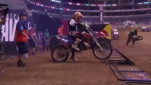A Red Bull Sign Is In The Background Of A Dirt Track GIF