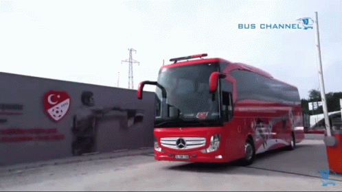 a red bus is parked in front of a wall with a c and a soccer ball on it