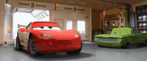 A Red Car And A Green Car Are Parked In Front Of A Paint Booth . GIF