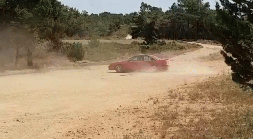 A Red Car Driving Down A Dirt Road With Trees In The Background GIF