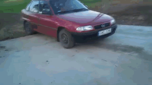 A Red Car Is Behind A Opel Logo On A Concrete Surface GIF
