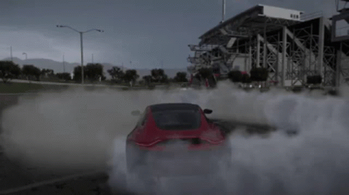 A Red Car Is Drifting In A Parking Lot With Smoke Coming Out Of The Tires GIF