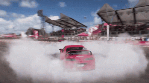 A Red Car Is Drifting On A Race Track With Smoke Coming Out Of It GIF