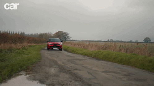 A Red Car Is Driving Down A Dirt Road With Car Written On The Bottom Right GIF