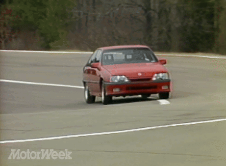 A Red Car Is Driving Down A Road With Motorweek Written In The Corner GIF