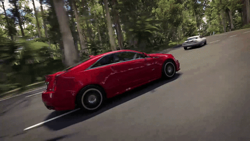 A Red Car Is Driving Down A Road With Trees On The Side GIF