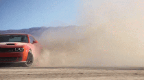 A Red Car Is Driving On A Dirt Road And Kicking Up Dust GIF