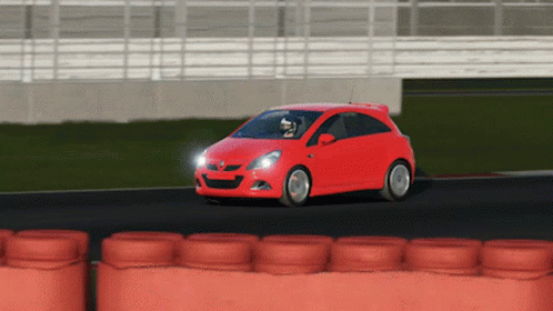 A Red Car Is Driving On A Track With A Row Of Orange Tires Behind It GIF